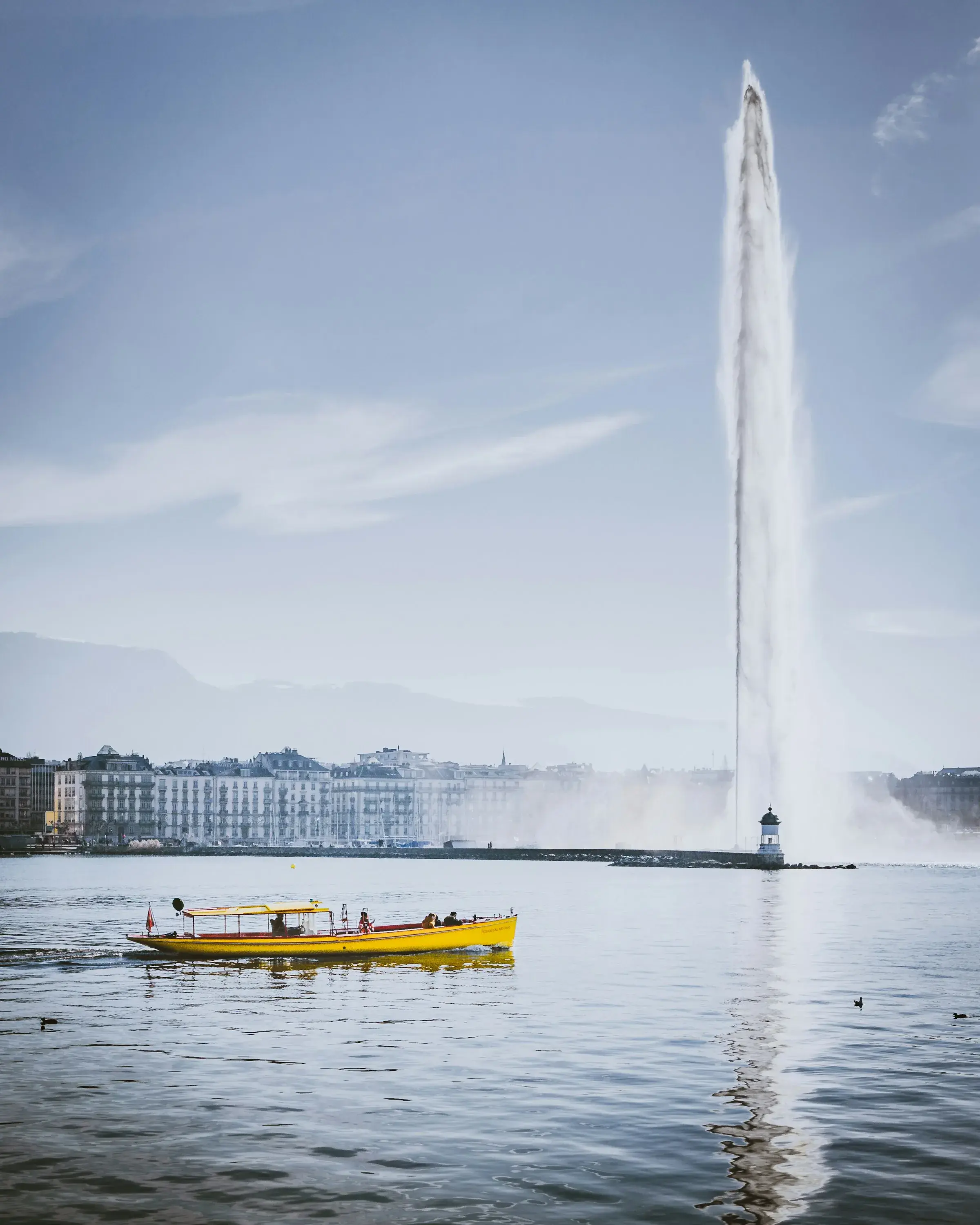 The Jet d’Eau rising over Lake Geneva, with a yellow Mouette boat crossing the water